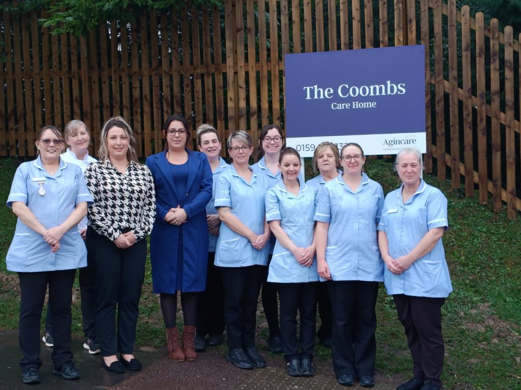 Picture of staff next the sign outside The Coombs Care Home in Coleford
